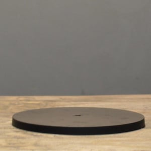 May include: A round, dark brown wooden serving tray. The tray is circular with a flat surface and a slightly raised edge. It sits on a light-colored wooden surface, with a gray background.