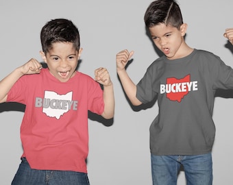 May include: Two children wearing red and grey t-shirts with the word "BUCKEYE" and the outline of Ohio. The children are wearing blue jeans and are making excited gestures.