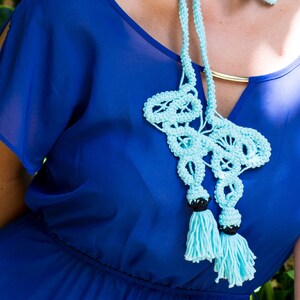 Pu&ograve; includere: Una collana di uncinetto blu chiaro con perline nere e nappe. La collana &egrave; indossata da una persona che indossa un abito blu reale.