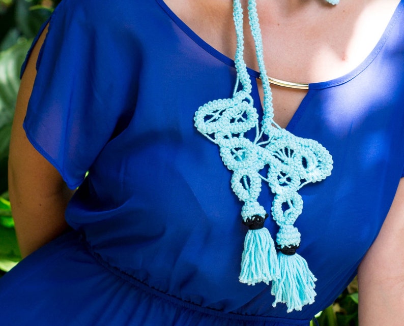 Pu&ograve; includere: Una collana di uncinetto blu chiaro con perline nere e nappe. La collana &egrave; indossata da una persona che indossa un abito blu reale.