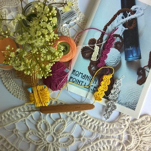 Peut inclure: Un ensemble de fournitures de crochet comprenant un crochet en bois de 1,0 mm, diverses pelotes de fil colorées en jaune, orange et magenta, un napperon en dentelle blanche et un livre intitulé ROMANIAN POINT LACE avec une bouteille bleue et des fleurs.
