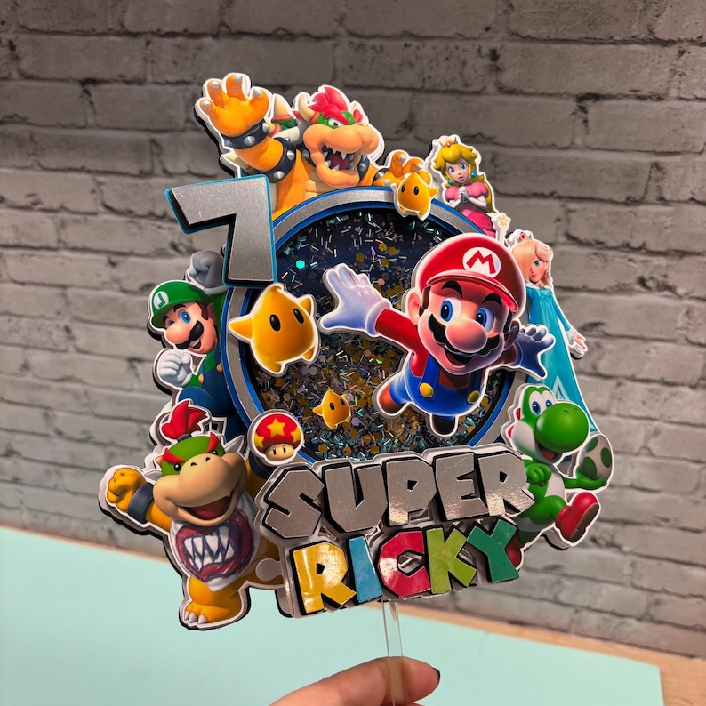 May include: A colorful cake topper featuring Mario, Luigi, Bowser, Princess Peach, Yoshi, and other characters. The number 7 is displayed, along with the text "SUPER RICKY". The topper is designed with a glittery, blue-toned background.