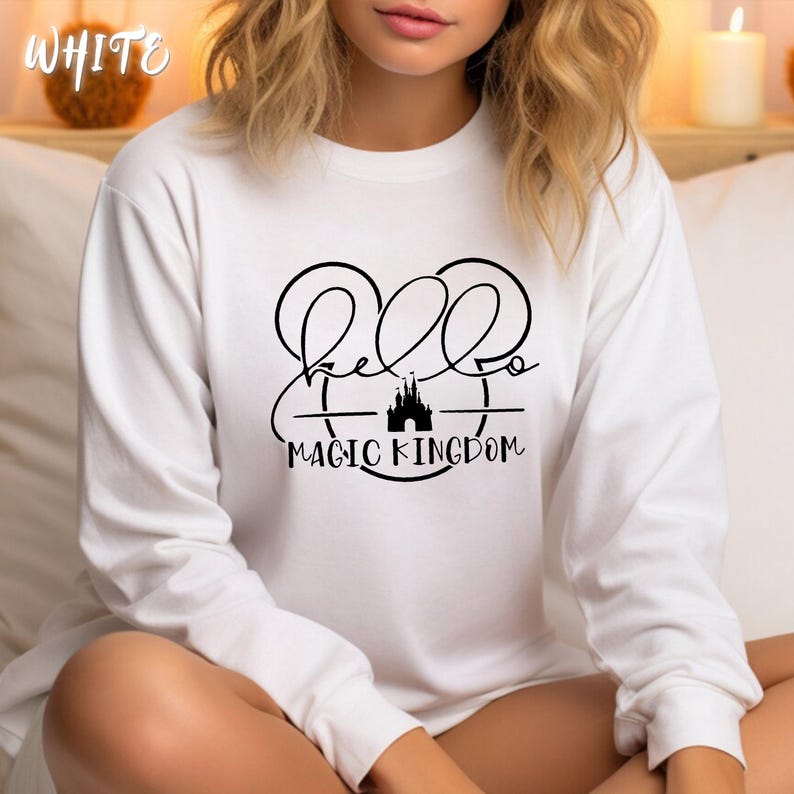 May include: White long-sleeve shirt with a black graphic that says "Hello Magic Kingdom" with a castle silhouette. The word "WHITE" is in the top left corner of the image.