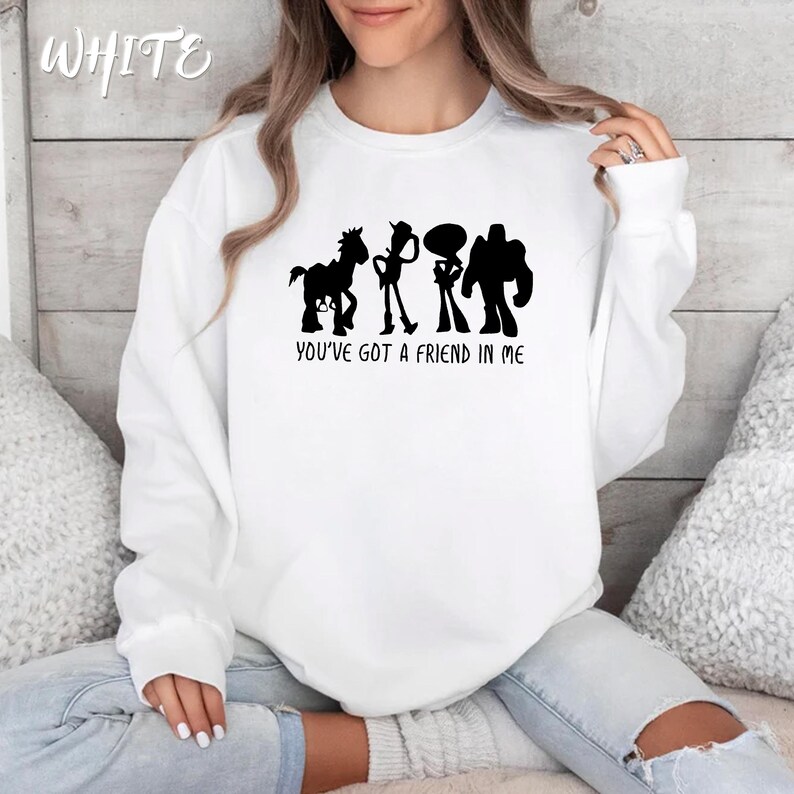 May include: White sweatshirt featuring a black silhouette of four animated characters with the text "YOU'VE GOT A FRIEND IN ME" below. The word "WHITE" is printed in cursive at the top left corner of the sweatshirt.