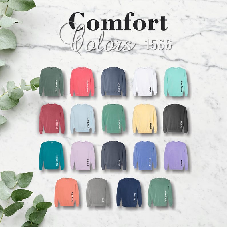 May include: A selection of Comfort Colors 1566 crewneck sweatshirts in various colors, including blue spruce, watermelon, blue jean, white, chalky mint, crimson, chambray, and more. The sweatshirts are displayed on a marble background.