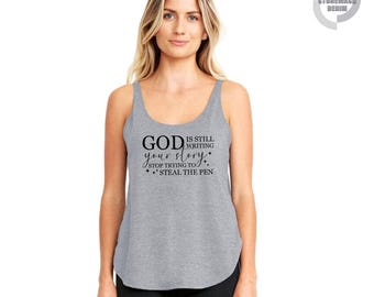 May include: A gray tank top with the text "GOD is still writing your story, stop trying to steal the pen" in black. The tank top has a scoop neck and a curved hemline. The brand name "STONEWASH DENIM" is printed on the upper right corner.