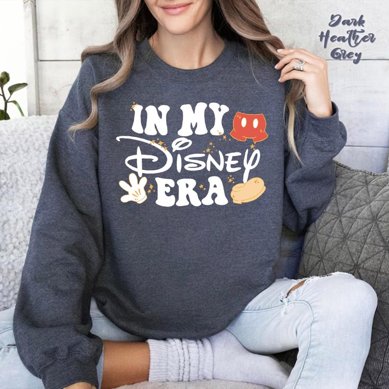 May include: Dark heather grey sweatshirt with the text "IN MY Disney ERA" in white, with Mickey Mouse-themed graphics. The sweatshirt has a crew neck and long sleeves. The text "Dark Heather Grey" is printed in the upper right corner.