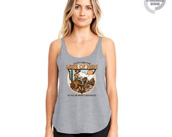 May include: Gray tank top with a graphic of a cowboy riding a horse in a desert scene. The text on the shirt reads "I DON'T NEED THE LAWS OF MAN TO TELL ME WHAT OUGHTA DO."