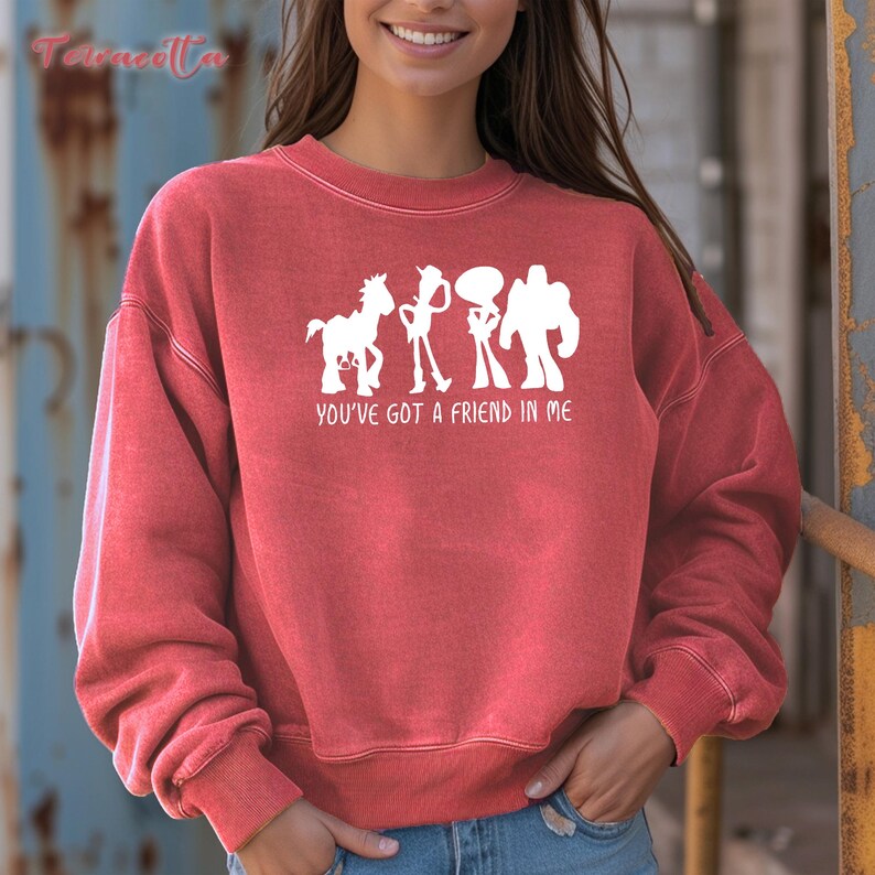 May include: Red sweatshirt with a white graphic of cartoon characters and the text "YOU'VE GOT A FRIEND IN ME". The sweatshirt is a solid red color and has a crew neck.