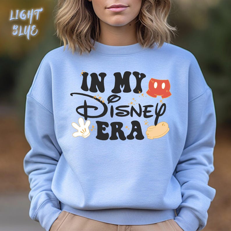May include: Light blue sweatshirt with the text "IN MY Disney ERA" in black, with Mickey Mouse-themed graphics in red, white, and yellow. The words "LIGHT BLUE" are in the upper left corner.