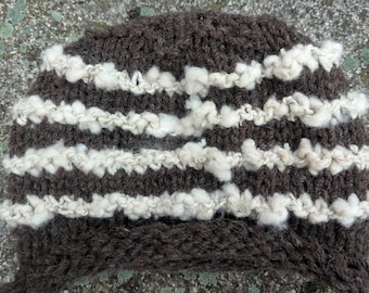 May include: A dark brown knitted hat with white, textured horizontal stripes. The hat is made from thick yarn, suitable for cold weather. The hat is a beanie style.