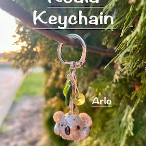 May include: A koala keychain with a silver keyring. The koala is gray with black eyes and tan ears. The keychain has green and yellow accents and the name "Arlo". The text "Koala Keychain" is at the top.