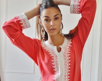 May include: A coral pink long-sleeved dress with white lace trim and pearl-like buttons down the front.