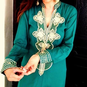 May include: A teal blue long-sleeved tunic with gold and green embroidery. The embroidery features a floral design and is beaded.