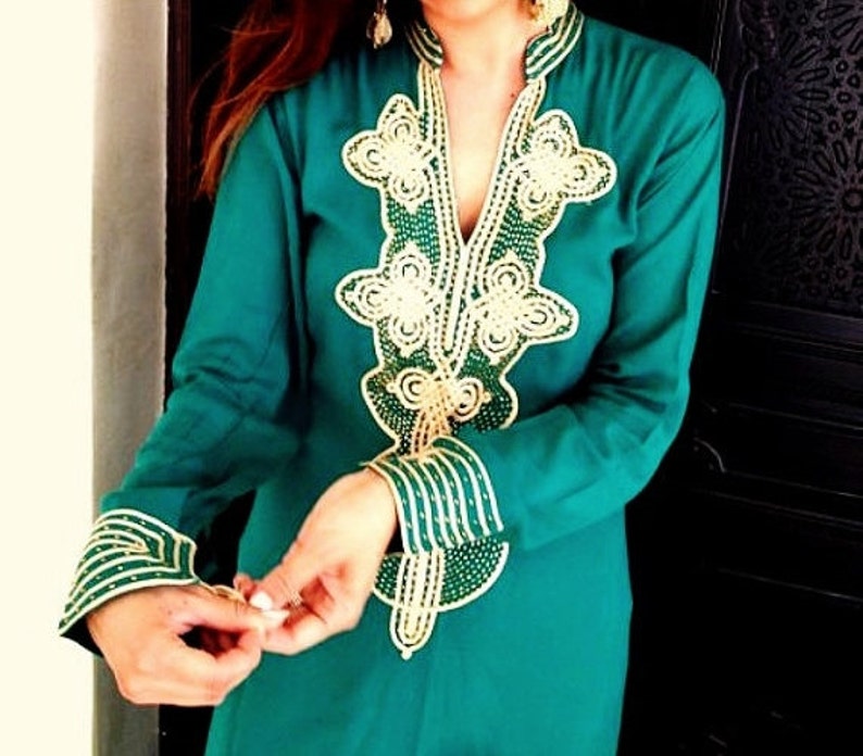 May include: A teal blue long-sleeved tunic with gold and green embroidery. The embroidery features a floral design and is beaded.