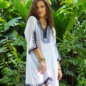 May include: A white, loose-fitting, embroidered dress with a V-neckline and 3/4 sleeves. The dress has a blue embroidered design and a lace trim at the neckline.