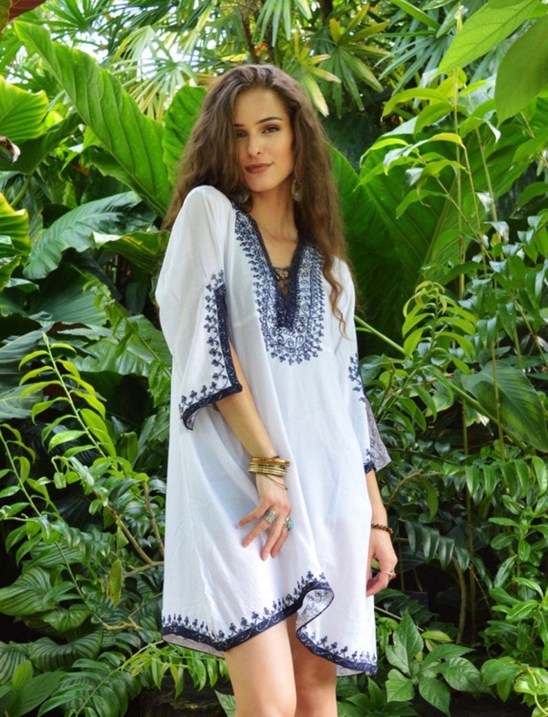 May include: A white, loose-fitting, embroidered dress with a V-neckline and 3/4 sleeves. The dress has a blue embroidered design and a lace trim at the neckline.