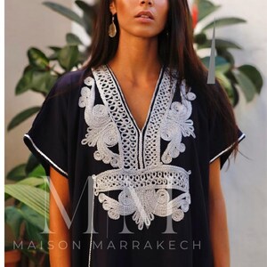 May include: A black kaftan with silver embroidery. The embroidery features a floral design and the text "Maison Marrakech".