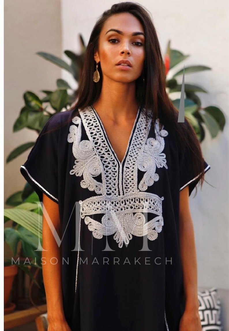 May include: A black kaftan with silver embroidery. The embroidery features a floral design and the text "Maison Marrakech".
