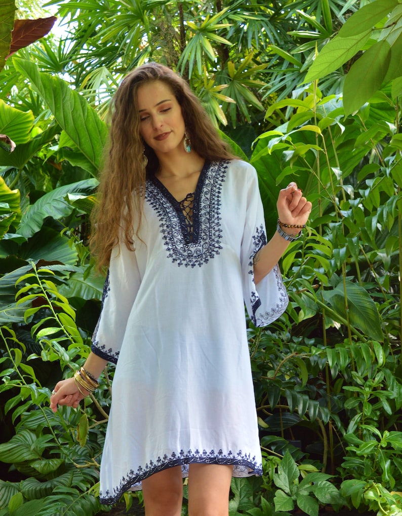 May include: White cotton tunic dress with blue embroidery and a lace-up neckline. The dress has a loose fit and 3/4 sleeves.