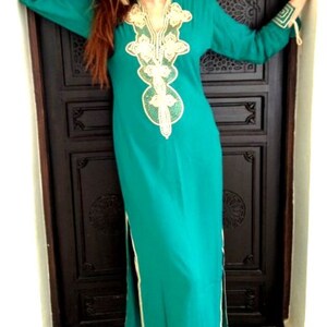 May include: A long, teal blue dress with a gold and white embroidered neckline. The dress has a side slit and a long sleeve.