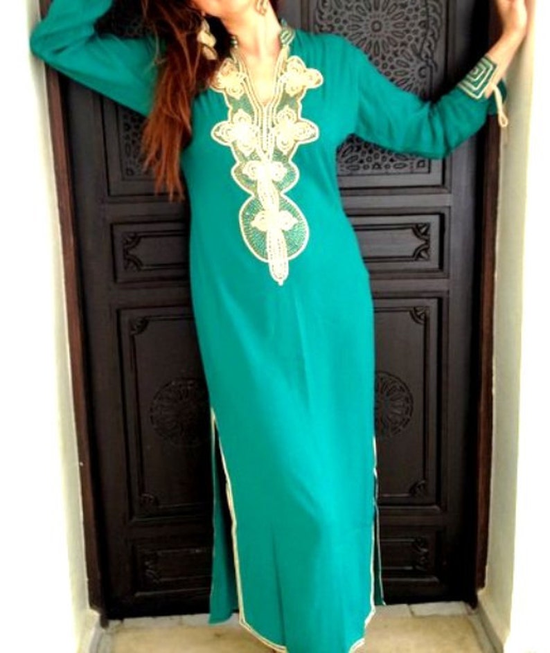 May include: A long, teal blue dress with a gold and white embroidered neckline. The dress has a side slit and a long sleeve.