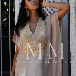 May include: A beige kaftan with gold embroidery and the text "MM MAISON MARRAKECH".