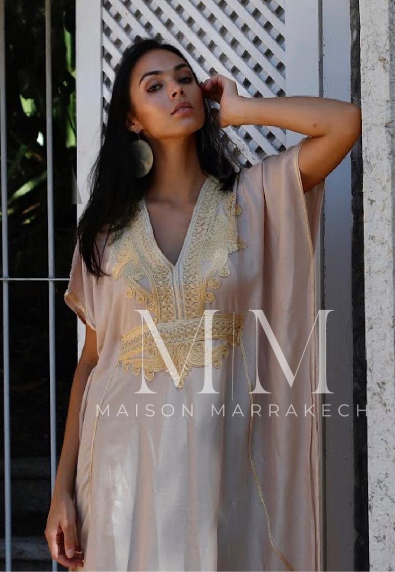 May include: A beige kaftan with gold embroidery and the text "MM MAISON MARRAKECH".