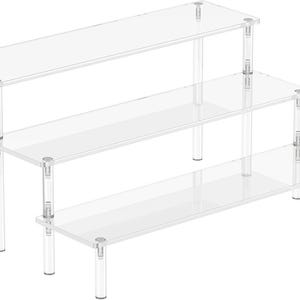 May include: Three-tier acrylic display stand with clear shelves and clear legs. The stand is made of durable acrylic and is perfect for displaying small items.