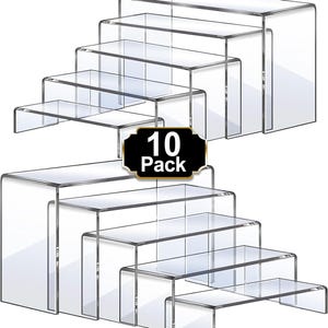 May include: Clear acrylic display risers in a set of ten. The risers are in a stepped design, perfect for showcasing small items. The set includes various sizes, offering versatility for product display. The label on the image reads "10 Pack".