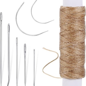 May include: A collection of sewing needles in various sizes and shapes, including curved and straight needles, alongside a spool of tan thread. The needles are silver, and the thread is wound around a white spool.