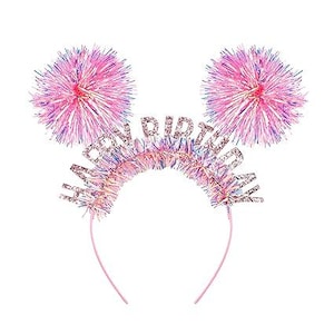 Może przedstawiać: Różowa opaska do włosów z puszystymi pomponami po obu stronach i napisem "Happy Birthday" w złotym brokacie.