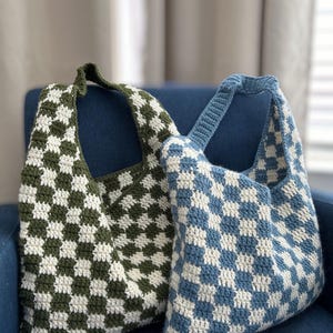 Peut inclure: Deux sacs fourre-tout crochet&eacute;s &agrave; la main. L'un est &agrave; carreaux vert olive et blanc, l'autre &agrave; carreaux bleu et blanc. Les deux sacs ont une seule bandouli&egrave;re et sont pos&eacute;s sur une chaise bleue.