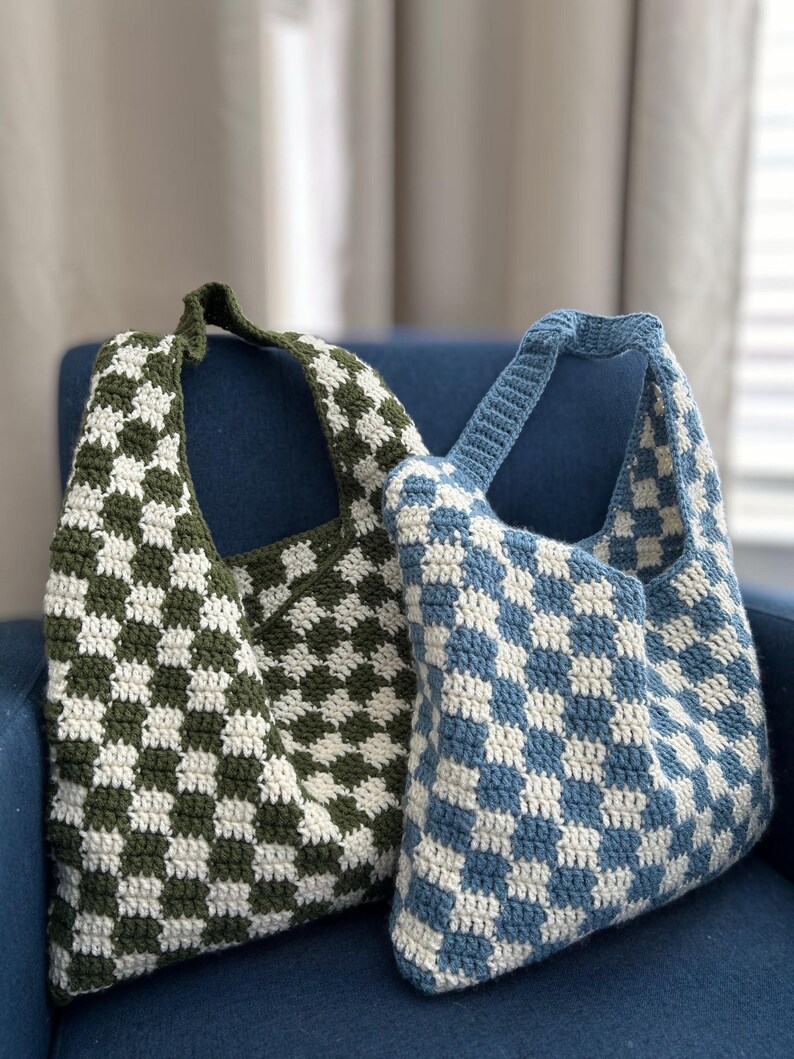Peut inclure: Deux sacs fourre-tout crochet&eacute;s &agrave; la main. L'un est &agrave; carreaux vert olive et blanc, l'autre &agrave; carreaux bleu et blanc. Les deux sacs ont une seule bandouli&egrave;re et sont pos&eacute;s sur une chaise bleue.