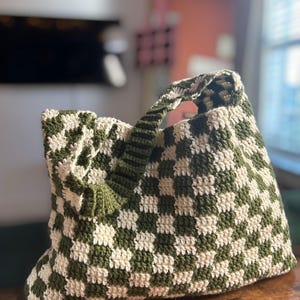 Peut inclure: Sac fourre-tout en crochet fait &agrave; la main avec un motif de damier vert olive et cr&egrave;me. Le sac est dot&eacute; d'une poign&eacute;e robuste et d'un int&eacute;rieur spacieux, parfait pour transporter l'essentiel. Le sac est fait de fil doux.