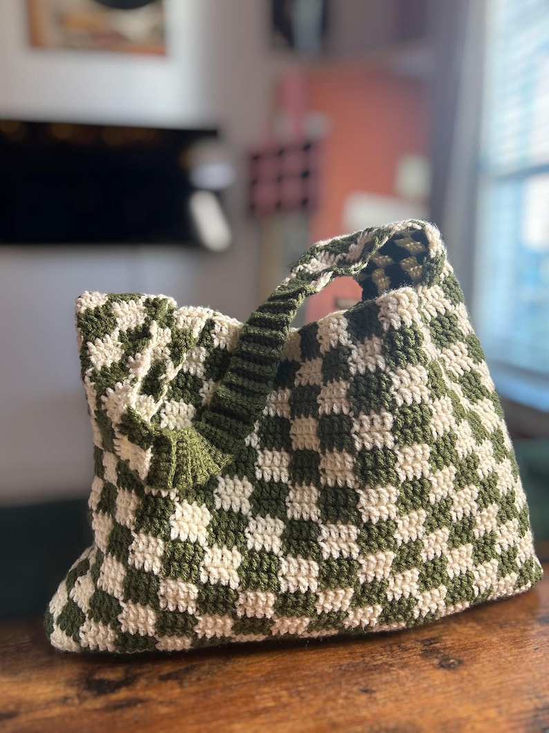 Peut inclure: Sac fourre-tout en crochet fait &agrave; la main avec un motif de damier vert olive et cr&egrave;me. Le sac est dot&eacute; d'une poign&eacute;e robuste et d'un int&eacute;rieur spacieux, parfait pour transporter l'essentiel. Le sac est fait de fil doux.