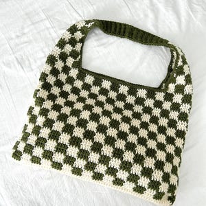 Peut inclure: Un sac fourre-tout crochet&eacute; &agrave; la main avec un motif en damier. Le sac pr&eacute;sente des carr&eacute;s altern&eacute;s vert olive et cr&egrave;me. La poign&eacute;e est de couleur vert olive uni. Le sac est fait d'un fil doux et textur&eacute;.