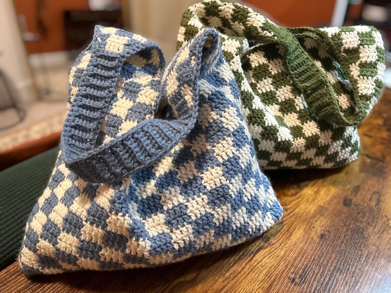 Peut inclure: Deux sacs fourre-tout crochet&eacute;s &agrave; la main. L'un est &agrave; carreaux bleus et blancs, avec une sangle bleue assortie. L'autre est &agrave; carreaux verts et blancs, avec une sangle verte. Les deux sacs sont pos&eacute;s sur une surface en bois.