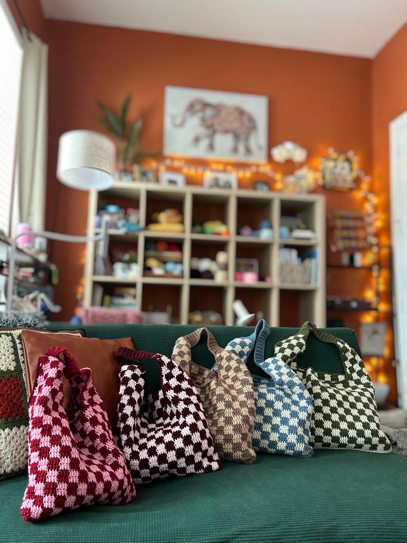 Peut inclure: Cinq sacs fourre-tout tricot&eacute;s &agrave; motif de damier, de couleurs rose, bordeaux, beige, bleu et vert. Les sacs sont faits &agrave; la main et sont pr&eacute;sent&eacute;s sur un canap&eacute; vert.