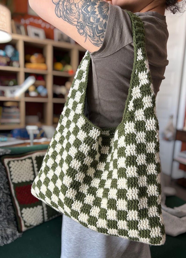 Peut inclure: Un sac fourre-tout crochet&eacute; &agrave; la main avec un motif de damier vert et blanc. Le sac a une large bandouli&egrave;re et un int&eacute;rieur spacieux. Le sac est fait de fil doux et est parfait pour transporter des courses, des livres ou d'autres articles. Un accessoire &eacute;l&eacute;gant et pratique.