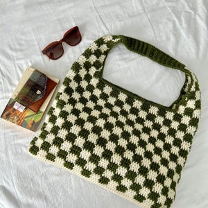 Peut inclure: Un sac fourre-tout crochet&eacute; &agrave; la main avec un motif &agrave; carreaux vert et cr&egrave;me. Le sac a une large bandouli&egrave;re. Sont &eacute;galement pr&eacute;sent&eacute;es des lunettes de soleil marron et un petit portefeuille avec un livre.