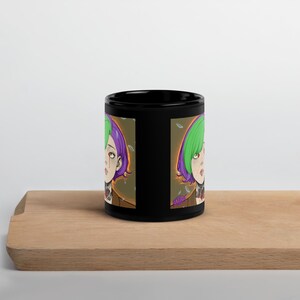 Może przedstawiać: Czarny ceramiczny kubek z kolorową ilustracją w stylu anime przedstawiającą osobę z zielonymi i fioletowymi włosami. Grafika powtórzona jest po obu stronach kubka. Kubek stoi na drewnianej powierzchni.