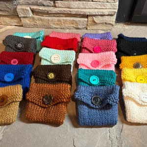 May include: A collection of 15 knitted coin purses in various colors, each with a button closure. The purses are arranged in three rows, with five purses in each row. The colors include blue, green, red, pink, brown, white, yellow, and black.