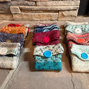 Könnte beinhalten: Eine Sammlung von gestrickten Beuteln mit verschiedenen farbigen Streifen und Knöpfen. Die Beutel sind aus verschiedenen Garnfarben hergestellt, darunter Blau, Grün, Rot, Weiß und Orange.
