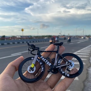 Könnte beinhalten: Schwarzes Miniatur-Fahrradmodell mit weißer Beschriftung "FACTOR" und "BLACK INC".