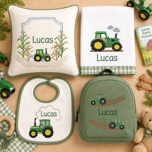 Puede incluir: Un conjunto de artículos personalizados para bebé que incluye un cojín cuadrado color crema, una toalla blanca de tejido tipo gofre con borde de cuadros vichy verdes, un babero blanco y una mochila verde salvia, todos con tractores verdes bordados y el nombre Lucas.