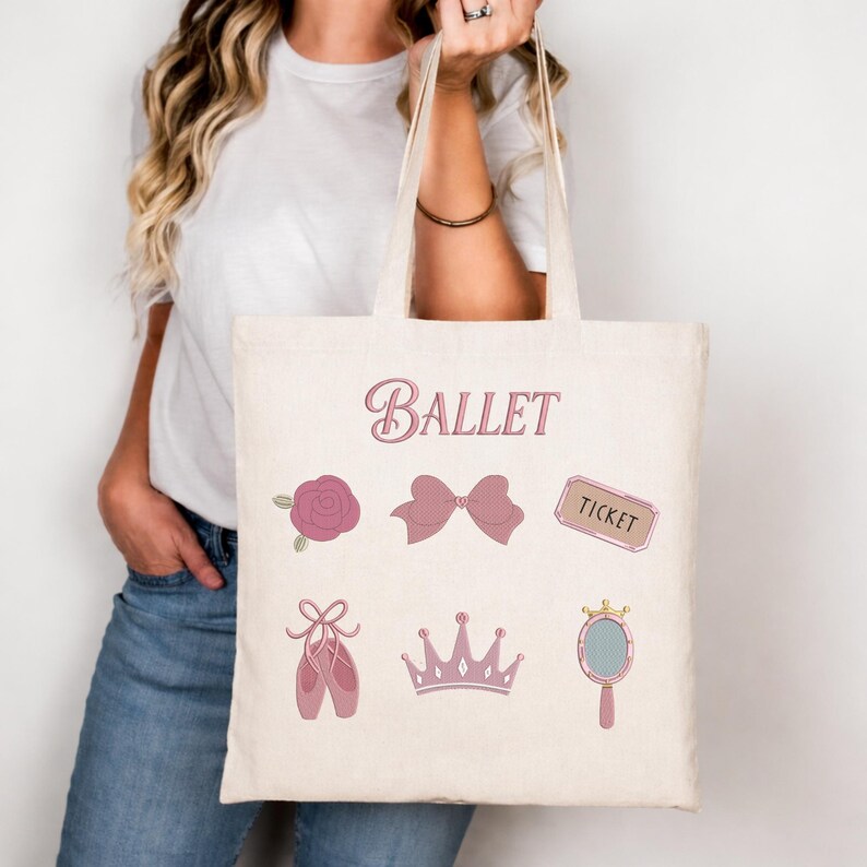 May include: A beige tote bag featuring the word "Ballet" in pink script. The bag is decorated with pink ballet-themed illustrations, including a rose, bow, ticket, pointe shoes, crown, and hand mirror. The bag is held by a person.
