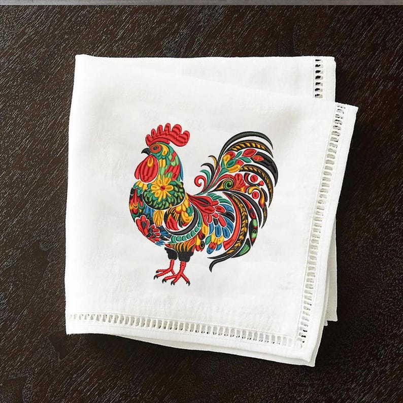 May include: White cloth napkin with a colorful embroidered rooster design. The rooster features red, yellow, blue, and green details. The napkin has a decorative, stitched border.