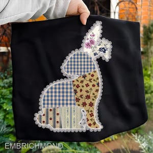 May include: Black fabric tote bag featuring a patchwork bunny design. The bunny is outlined with white lace and composed of various patterned fabrics, including gingham, floral, and striped patterns. The text "EMBRICHMOND" is visible at the bottom.