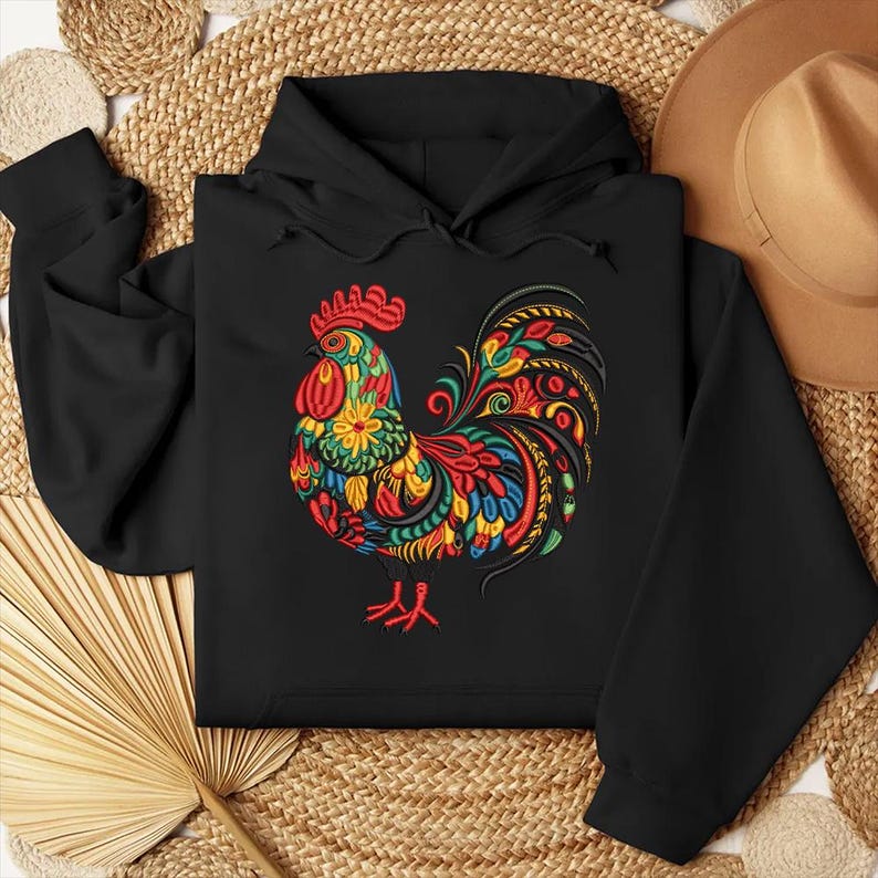 May include: Black hooded sweatshirt featuring a colorful rooster design. The rooster is adorned with red, yellow, green, and blue floral and patterned details. The design is centered on the front of the sweatshirt.